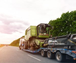 Heavy industrial truck with semi trailer platform transport disassembled combine harvester machine on common highway road on sunset or sunrise day. Agricultural equipment transportation service.